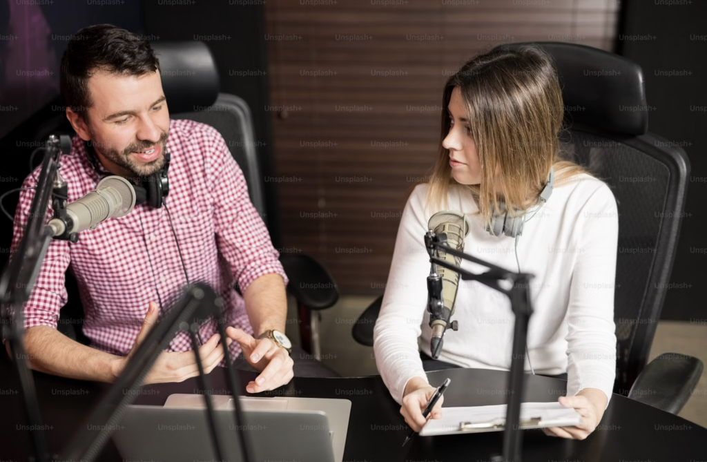 Two YouTube creators discussing YouTube scripts in a recording studio with microphones and a laptop.
